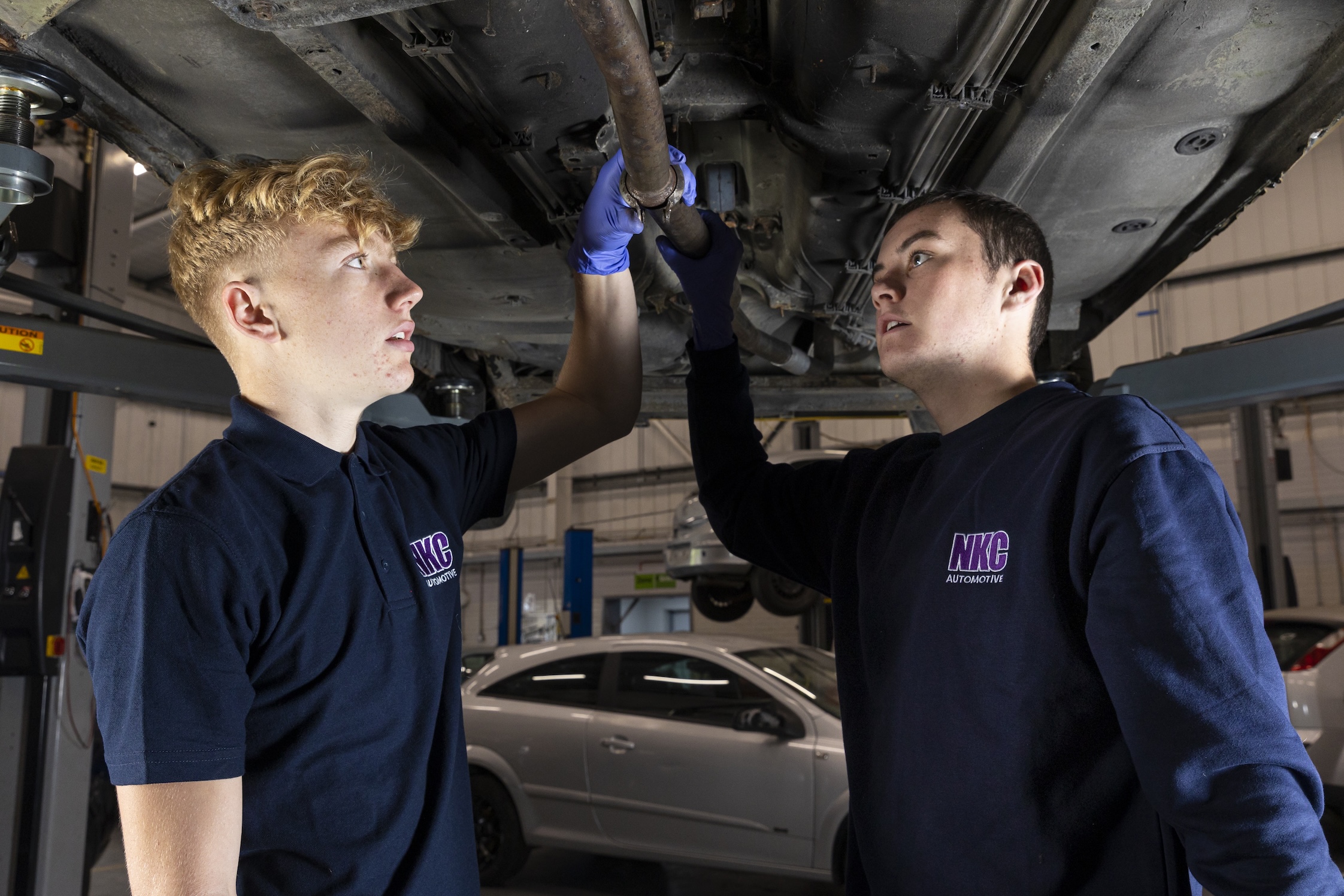 Two motor vehicle students looking at the underside of a car