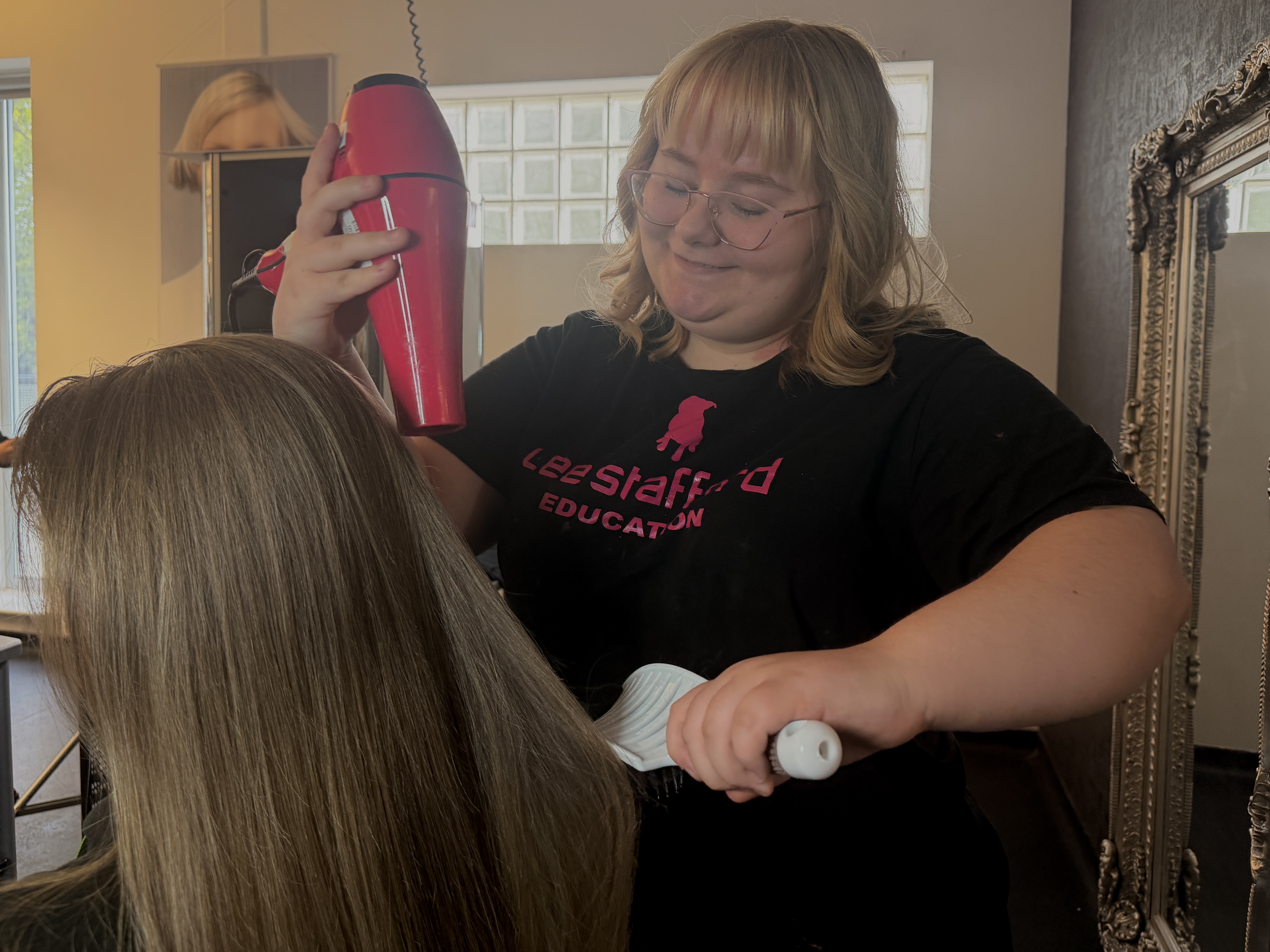 Student with hairdryer and brush doing model's hair