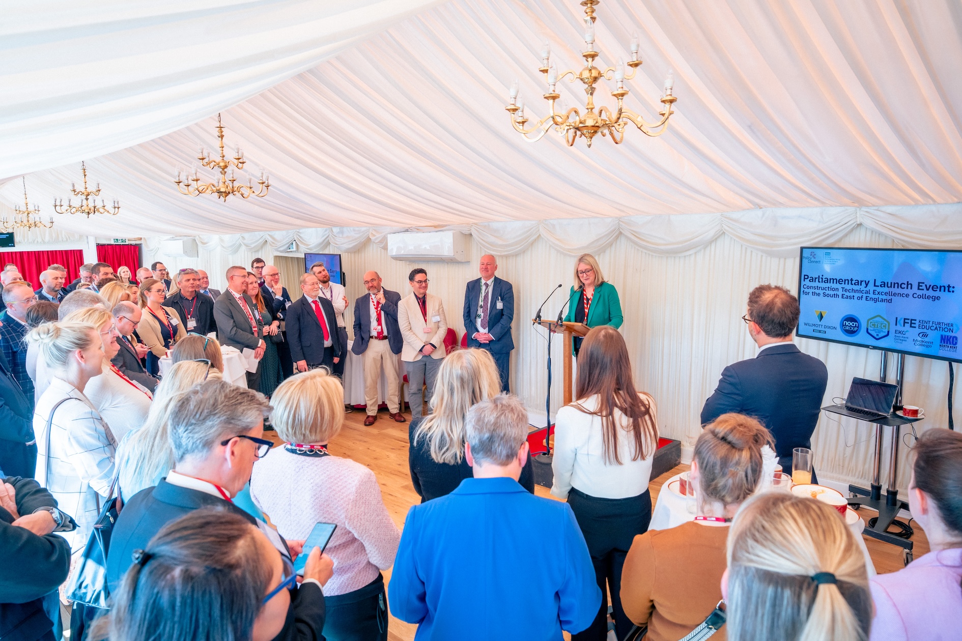 Group of people stood watching a speech being given from behind a lectern